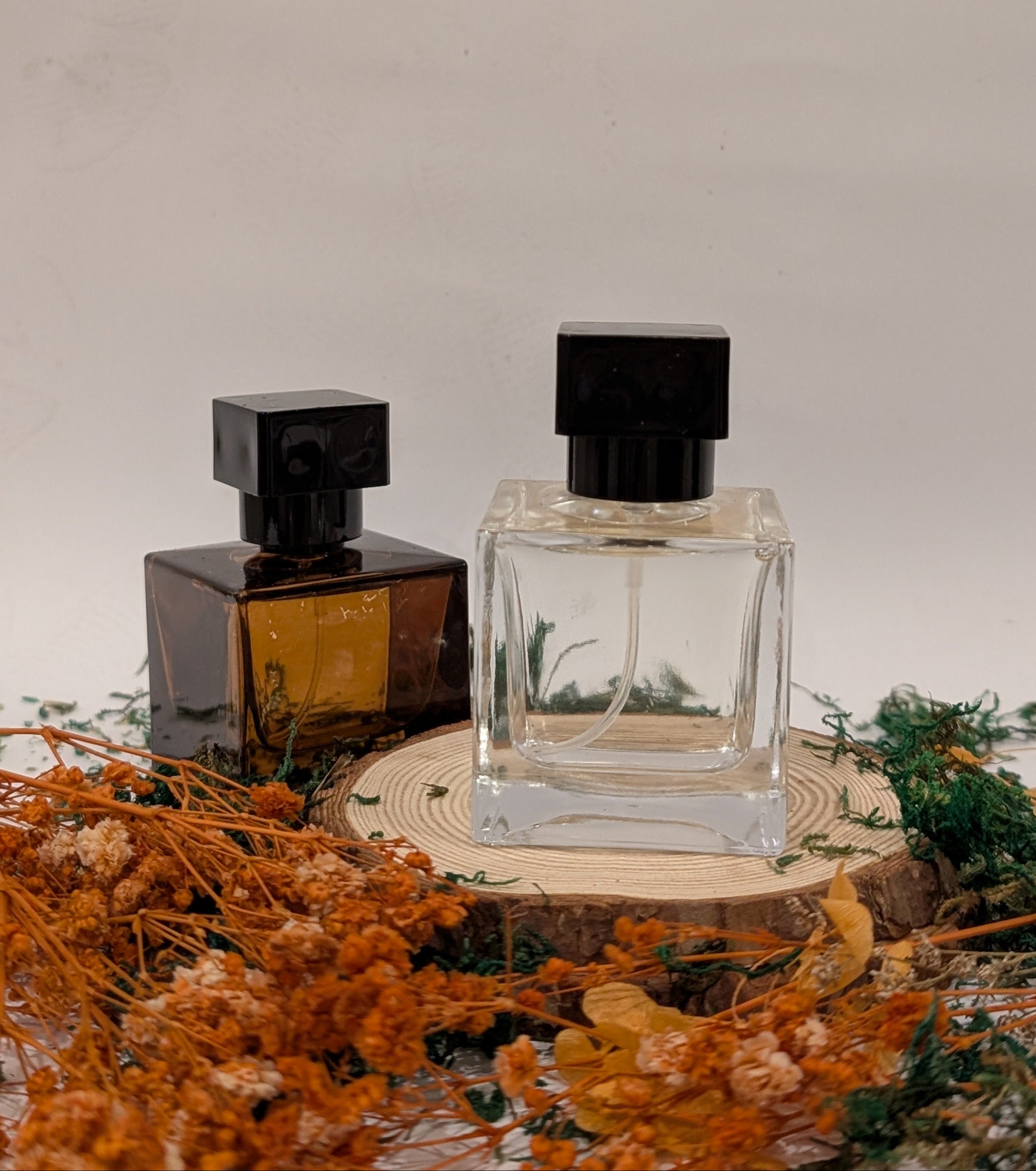Two perfume bottles on a wooden stand with dried flowers and greenery.